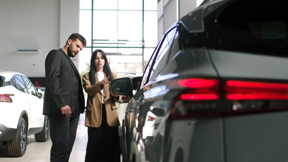 Stylish female car dealer serving a client in a car showroom.